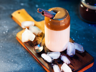 Wall Mural - A glass of Korean popular coffee drink. Whipped cream dalgona iced coffee. Cinnamon stick, chunks of ice on a wooden board
