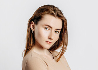 Wall Mural - Beautiful young girl smiling and posing looking at the camera on a white isolated background. Positive brunette woman in a beige jumper. Kind look.