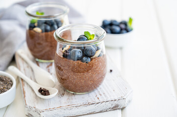 Chocolate chia pudding with blueberry, almonds and mint on top in a glass jar on a white wooden background. Healthy food. Copy space.