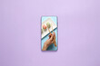 Female hand with chopsticks and sushi rolls on screen of mobile phone on color background