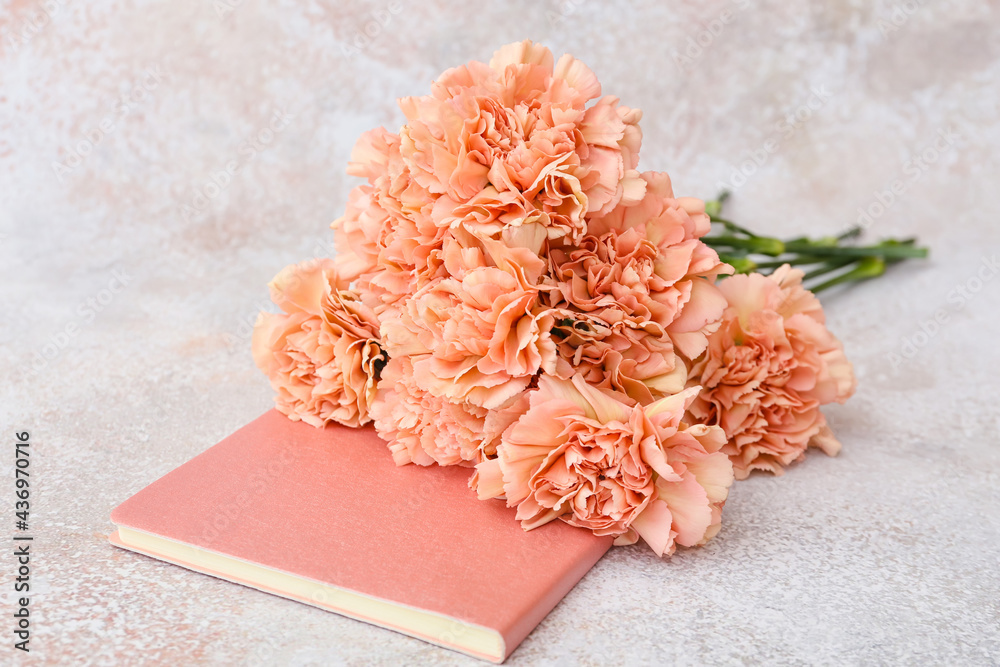 Beautiful carnation flowers and notebook on light background