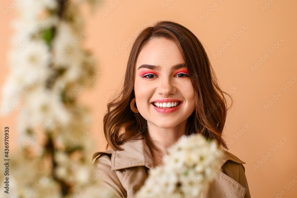 Beautiful young woman with blooming spring branches on color background