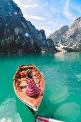 Poster - woman sitting in big brown boat at lago di braies lake in Italy