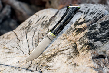 Handmade hunting knife among the stones in nature. Photo outside of a sharp homemade knife. A man's gift. Blade. Fishing. Picnic. Rest in the wild.