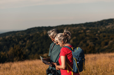 Wall Mural - Active senior couple hiking in nature with backpacks, enjoying their adventure at sunset.