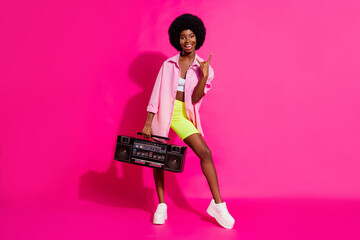 Photo of sweet rude dark skin woman dressed crop top showing har rock sign listening boombox isolated pink color background