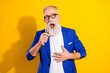 Photo of happy cheerful old man sing hold hand mic karaoke wear glasses isolated on yellow color background