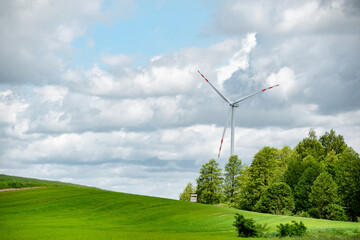 Ecological wind farm, windmill for electricity, against the background of a green field and clouds 