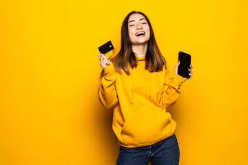 Young Asian woman using credit card and smart phone for online shopping, payment over yellow background