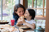 Fototapeta Tulipany - Mom and daughter eat pizza in a cafe, restaurant.