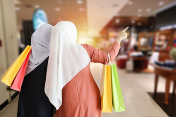 Rear view two young shopper muslim women holding shopping bags with shopping mall blurred background