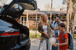 © gstockstudio - Happy young family with little packing stuff into the car and smiling while standing near house