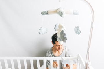 young adult man preparing and decorating the crib for the arrival of a baby. new son concept. parenting and preparations