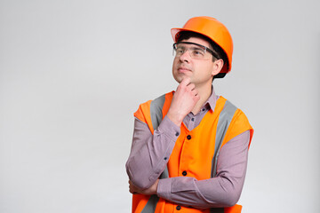 Young engineer in hard hat and reflective vest thinking on grey studio background, architect looks with an admiring inspired look