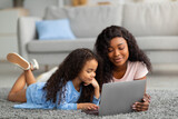 Fototapeta Londyn - Remote education. Cheerful black mom helping her little daughter with web lesson on laptop computer at home