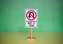 Closeup Of A Toy "NO U TURN" Sign On A Wooden Stand Against A Green Background