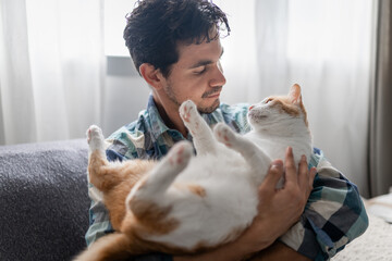 young man holds a brown and white cat in his arms