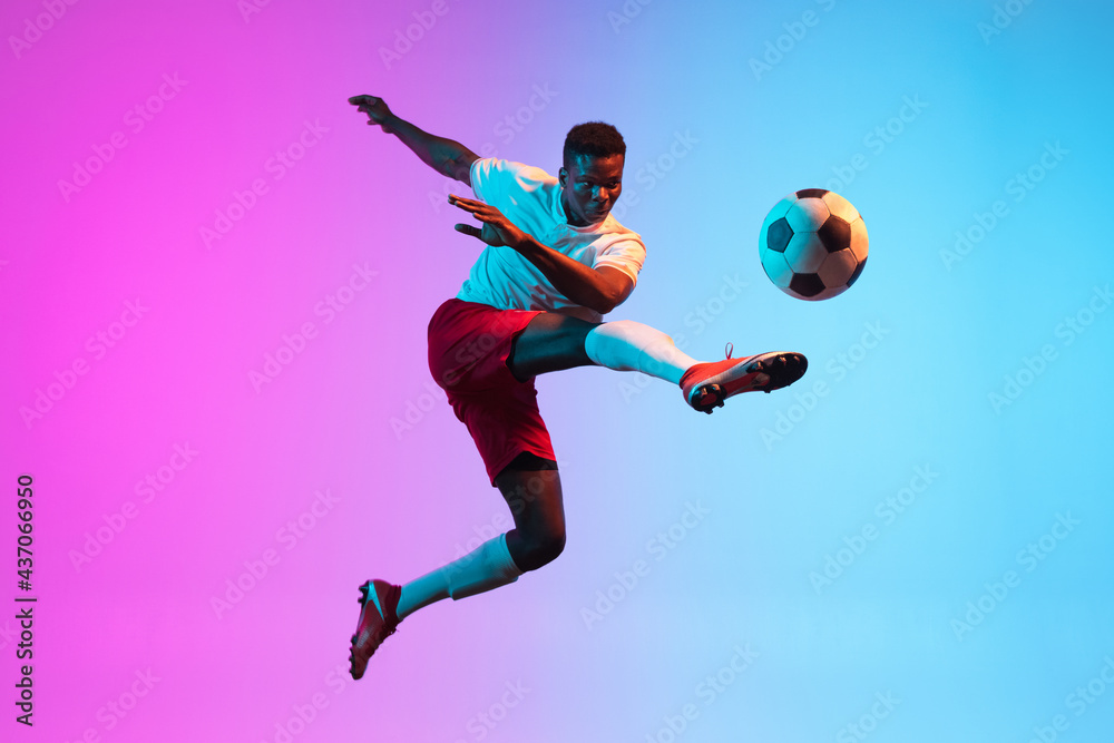 One African man, professional soccer football player training isolated on gradient blue pink background in neon light. - obrazy, fototapety, plakaty 