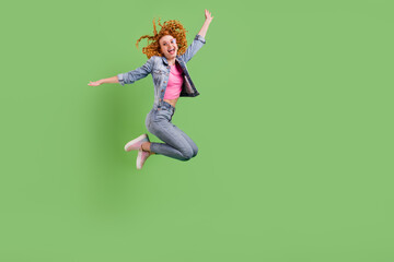 Wall Mural - Full length photo of playful sweet young woman wear jeans outfit spectacles jumping empty space smiling isolated green color background