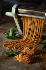 fresh orange spaghetti and two pasta nests on a wooden surface filled with flour, basil leaves and a rolling pin