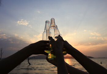 Close up group of tourist touch beverage bottle together cheer for happy moment at camping site, Cheer took bottles to collide, Group of teenage enjoy camping picnic , barbecue and drink at lake