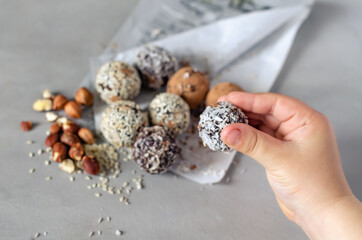 The child holds in his hand the Energy Bols - homemad raw,vegan candy. Mixed dates, nuts, dried fruits, sprinkled with coconut, cocoa and sesame seeds. The concept of healthy sweets. Paleo, keto diet