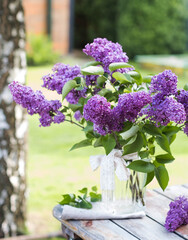 Beautiful bouquet of lilacs in a vase on a wooden table in nature.