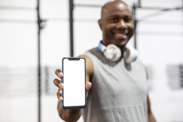 Black sportsman smiling showing the blank screen of a smartphone. Concept of sports apps. Selective focus. 