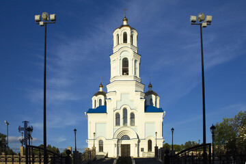 White Orthodox church with three golden domes against a blue sky with stratus clouds. 
The temple is part of the temple complex. A wide staircase leads to it. In the foreground, on both sides