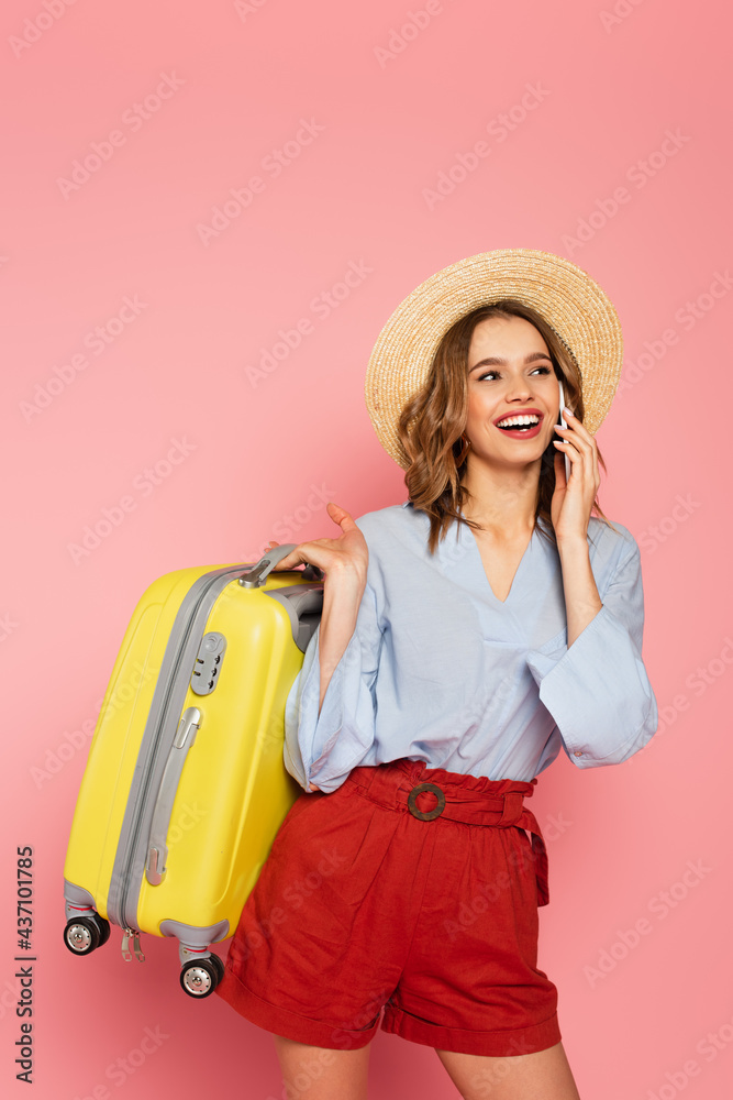 Pretty tourist with suitcase talking on smartphone on pink background - obrazy, fototapety, plakaty 