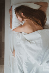 Beautiful girl with long hair sleeps in her bed on white sheets