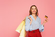 Cheerful woman with shopping bags holding credit card on pink background
