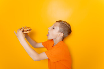 Wall Mural - a boy in an orange T-shirt stands sideways and holds a hamburger he wants to eat