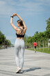 © Larysa - Back view young slim woman in sport clothes stretched with arms up standing on the alley of the city park. Healthy lifestyle, beautiful buttocks, outdoors workout, training alone, sport body concept .