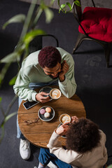 Overhead view of young african american coupe holding coffee cups during date in cafe