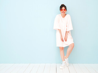 Wall Mural - Young beautiful smiling female in trendy summer hipster clothes. Sexy carefree woman posing near light blue wall in studio. Positive model having fun indoors. Cheerful and happy