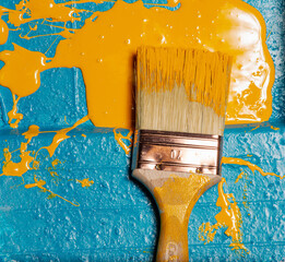 Poster - Vertical shot of a paintbrush with spilled yellow paint on a blue surface