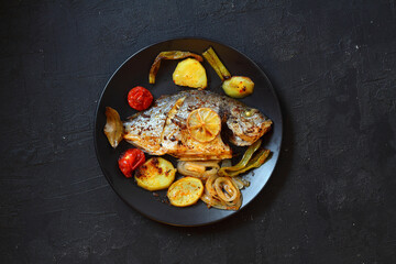 Wall Mural - Delicious grilled dorado or sea bream fish with salad, spices, grilled dorada on a black plate. Top view, overhead, copy space