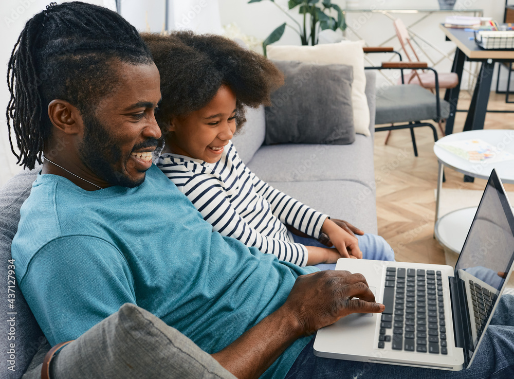 Father's day. Dad and daughter look at the laptop together and laugh. Fatherhood, happy family - obrazy, fototapety, plakaty 