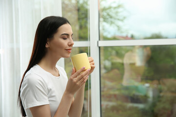 Wall Mural - Young woman with cup of drink relaxing near window home, space for text