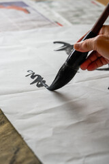 Wall Mural - a calligrapher is writing calligraphy characters with a large brush, a close-up of the brush. transl