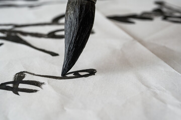 Wall Mural - a calligrapher is writing calligraphy characters with a large brush, a close-up of the brush. transl