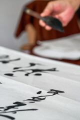 Wall Mural - a calligrapher is writing calligraphy characters with a large brush, a close-up of the brush. transl