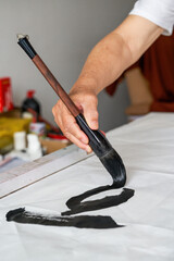 Wall Mural - a calligrapher is writing calligraphy characters with a large brush, a close-up of the brush. transl