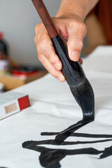 Wall Mural - a calligrapher is writing calligraphy characters with a large brush, a close-up of the brush. transl