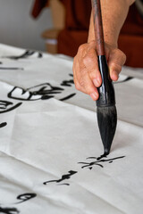 Wall Mural - a calligrapher is writing calligraphy characters with a large brush, a close-up of the brush. transl