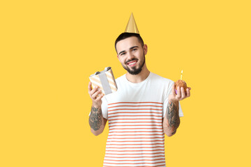 Poster - Happy young man with gift box and birthday cupcake on color background