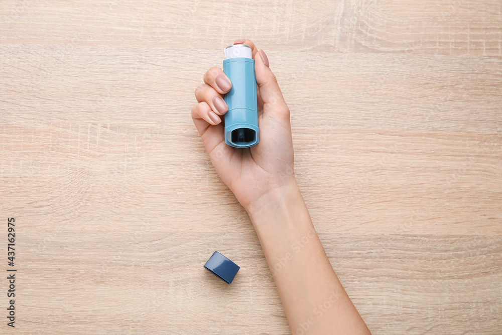 Woman with inhaler on light wooden background