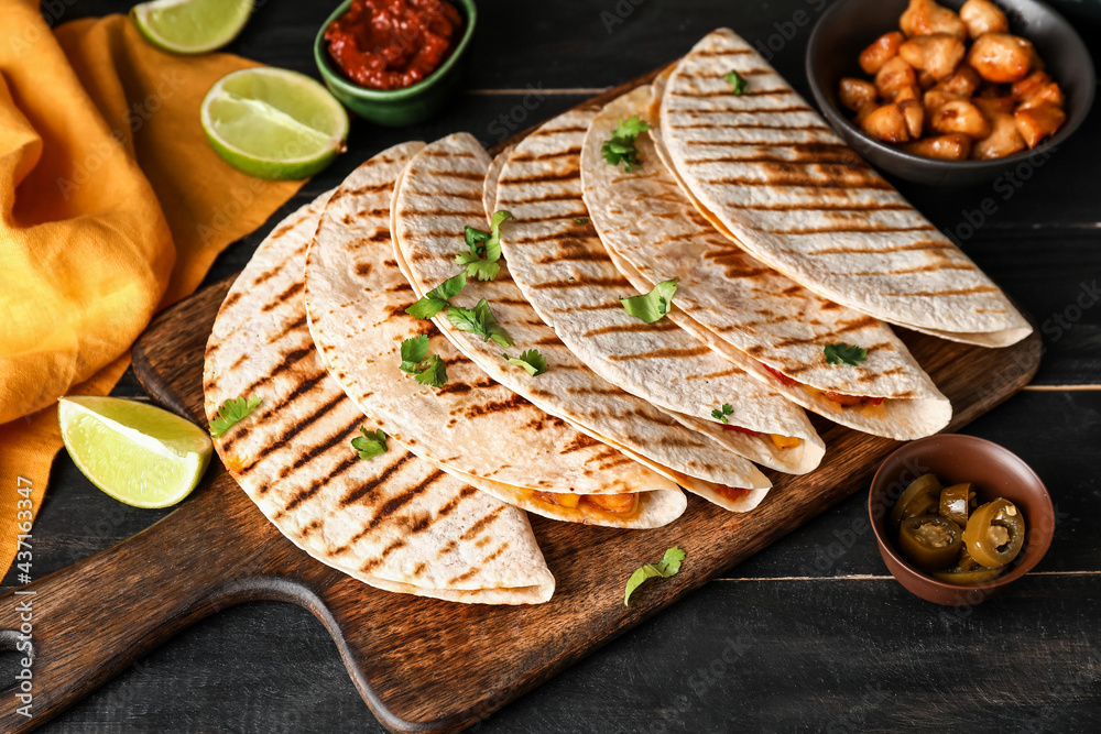 Board with tasty quesadillas on dark wooden background