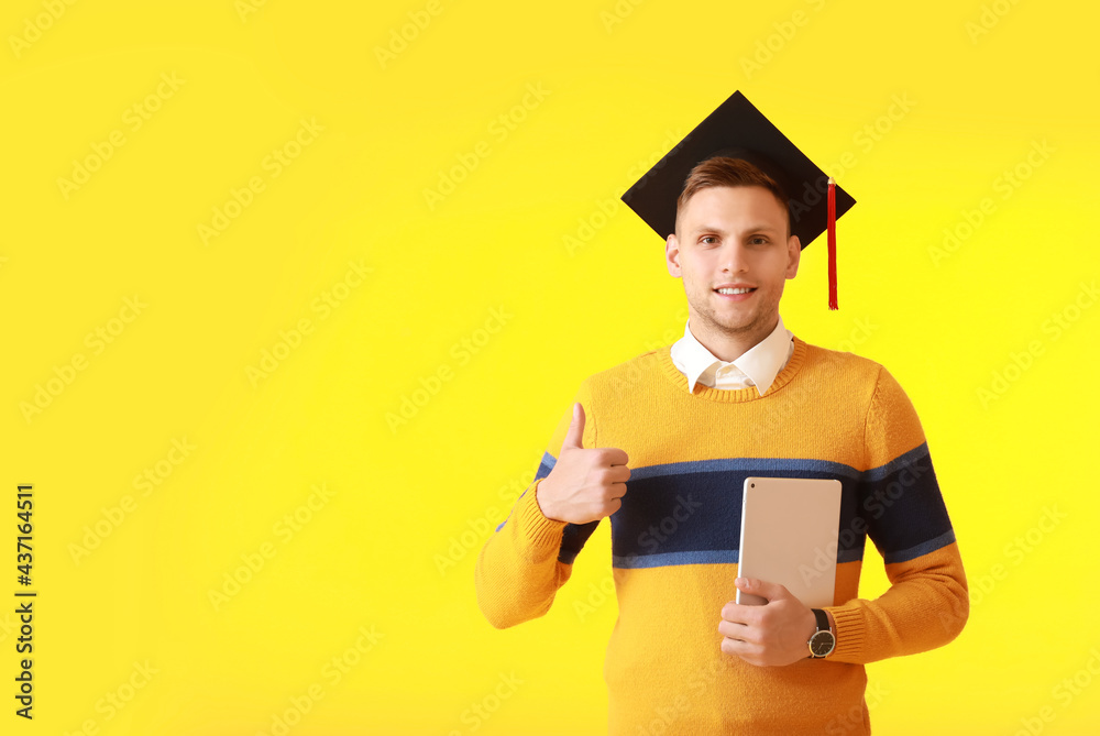 Male graduating student with tablet computer showing thumb-up on color background